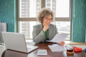 A mature woman who is an accountant is smiling as she goes through paperwork in an office setting.